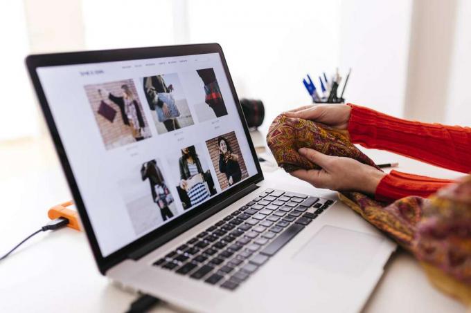 Kobieta trzymająca tkaninę przed laptopem z otwartą stroną modową