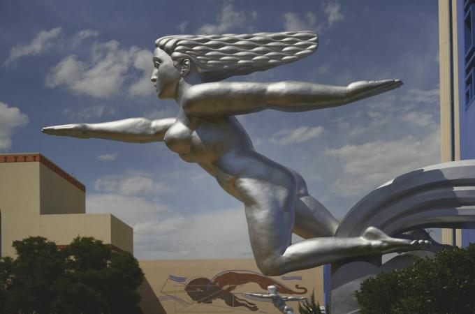 srebrna rzeźba nagiej kobiety, pozornie biegającej, włosy spływające z tyłu, jedno ramię do przodu i jedno ramię z tyłu